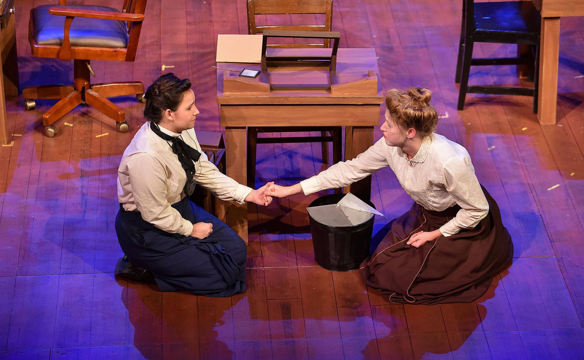Two female students holding hands on a stage