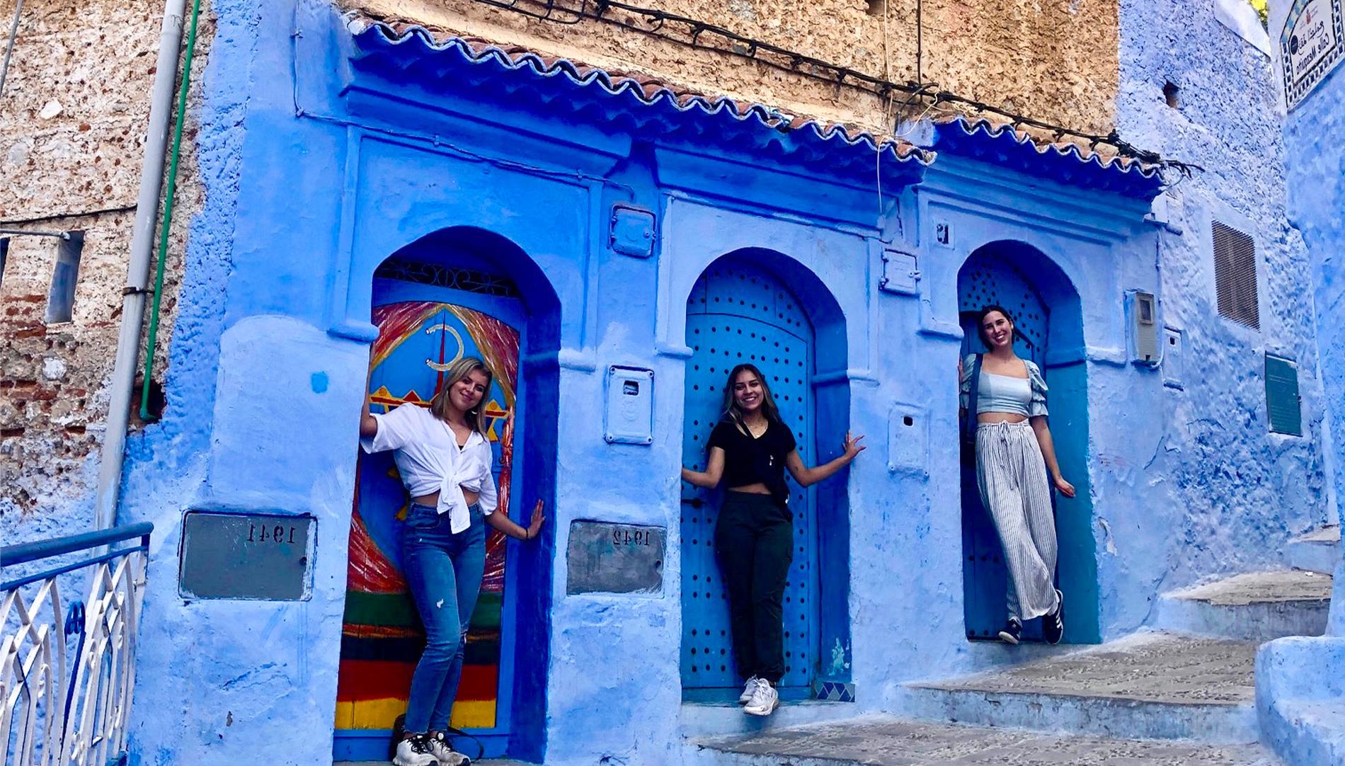 Three female students standing by blue architecture